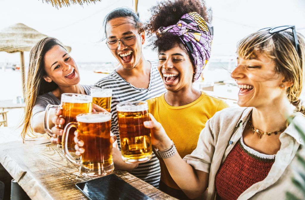 Happy tourists toasting beer glasses at kiosk cocktail beach bar